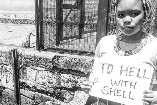 Black and white photo of a woman holding a sign that says 'to hell with shell'.